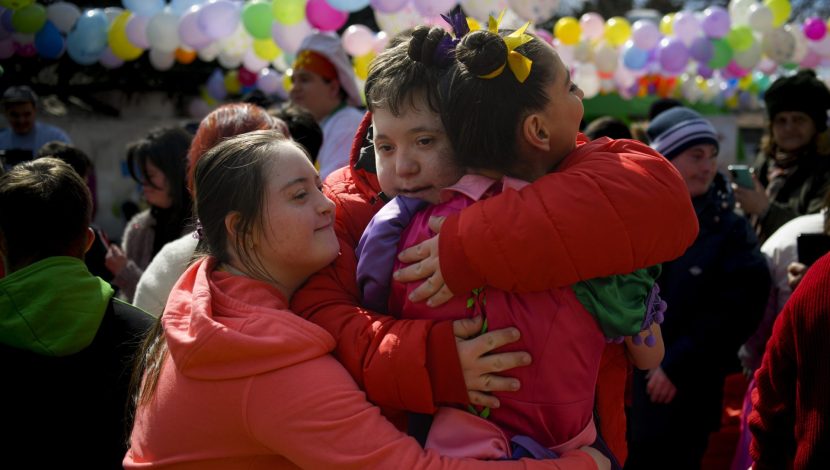 Tre ragazzi con disabilità intellettiva si abbracciano durante una manifestazione per il World Down Syndrome Day