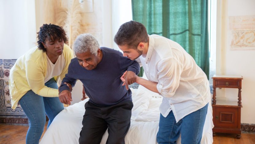 Un uomo e una donna aiutano un anziano ad alzarsi dal letto