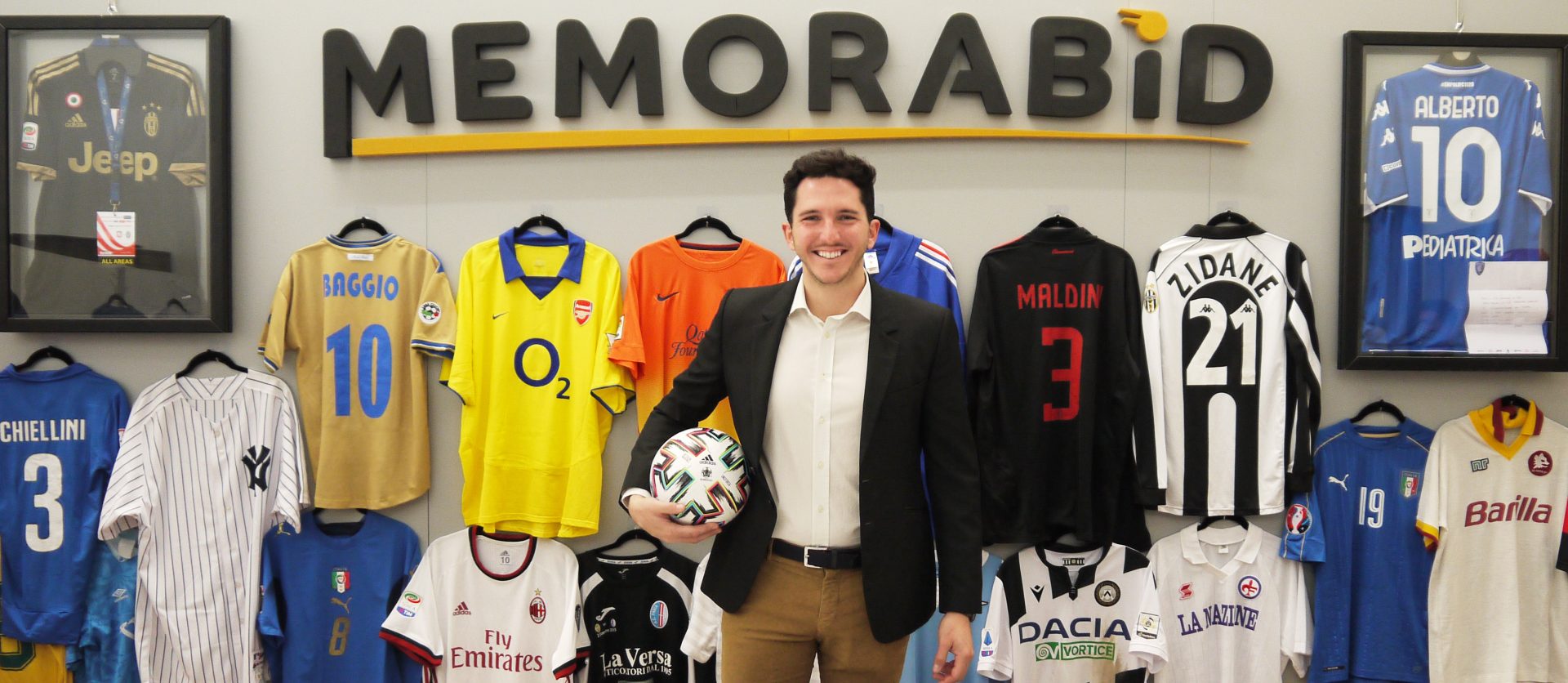 Alberto Zaccheti Ciriani con in mano un pallone da calcio, sullo sfondo la scritta "Memorabid" in alto e sotto magliette di calciatori appese