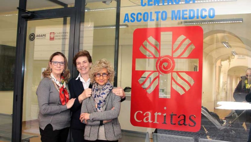 Tre persone davanti a una vetrina con scritto "Centro di ascolto medico" e sotto "Caritas