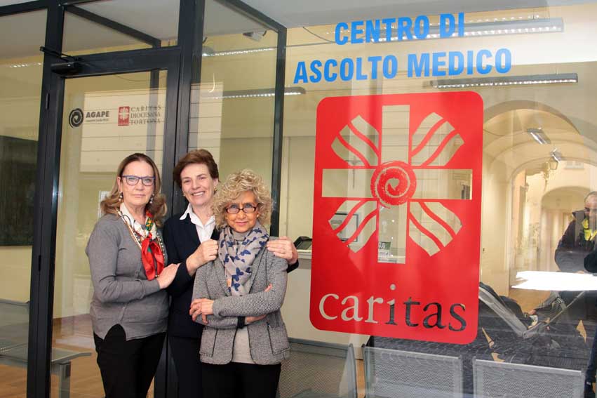 Tre persone davanti a una vetrina con scritto "Centro di ascolto medico" e sotto "Caritas