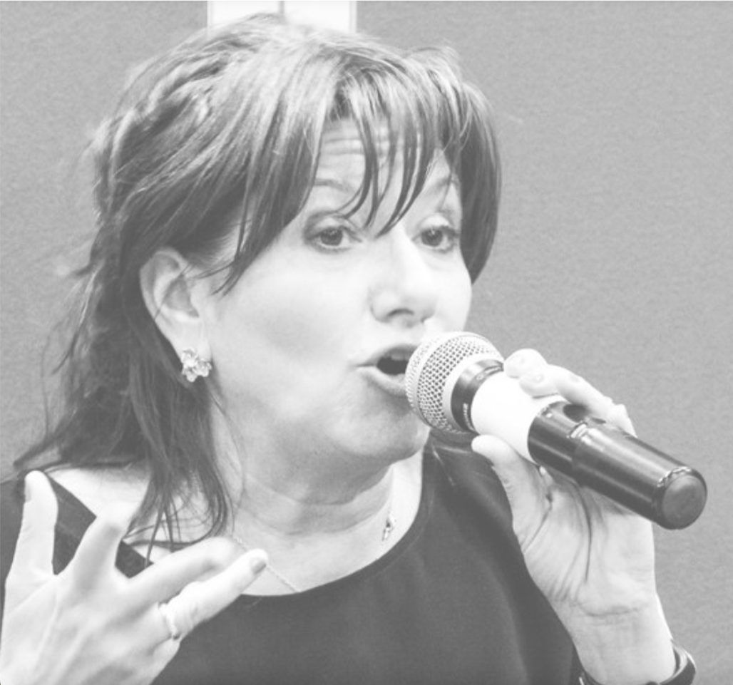 Una foto in bianco e nero di una persona che parla al microfono, presa dalle spalle in su, con la mano destra gesticola 