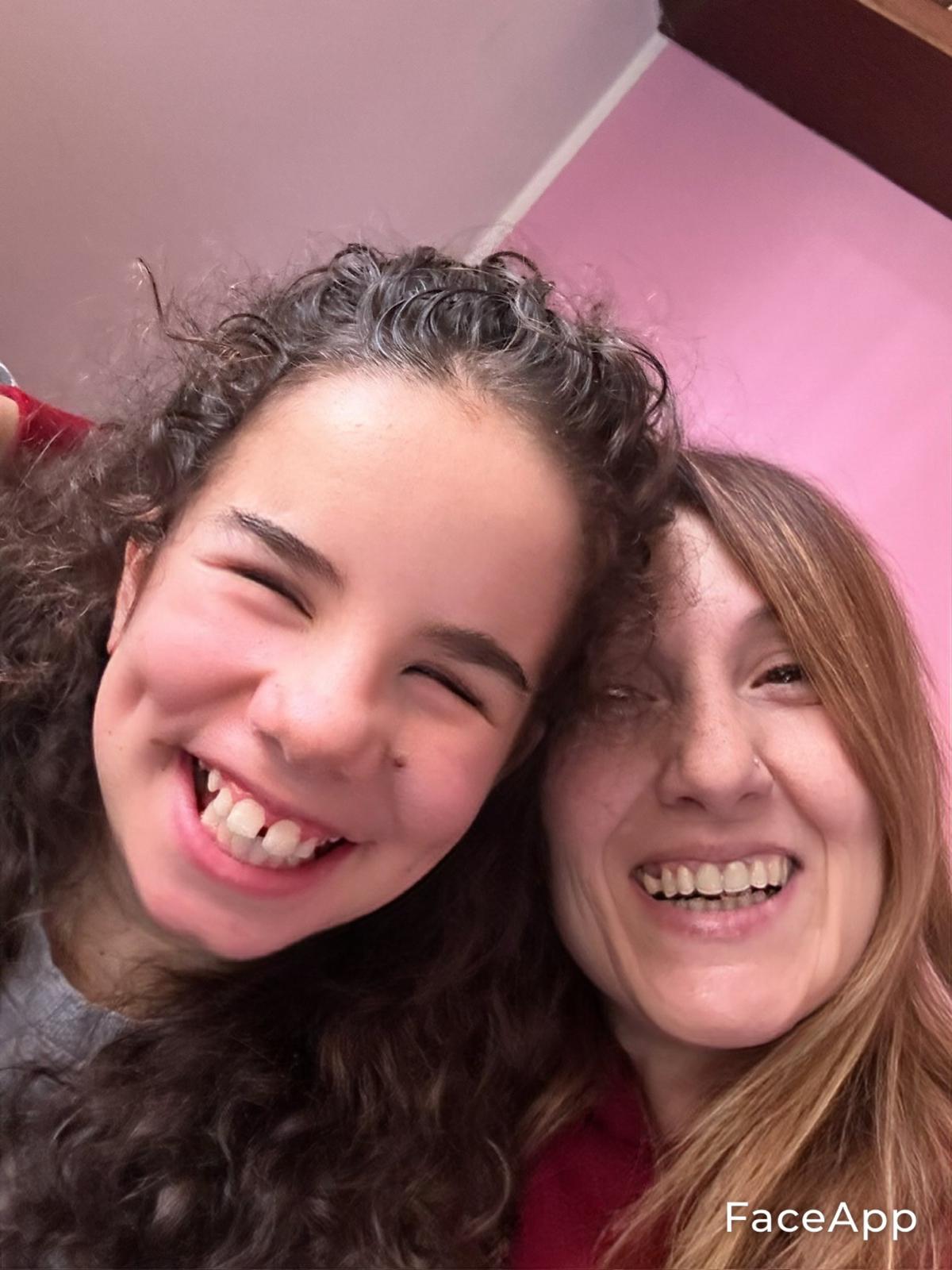 Due facce sorridenti in primo piano,una bimba mora e riccia e una mamma coi capelli castani