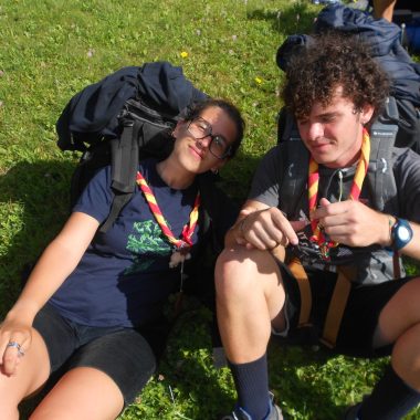 Un ragazzo e una ragazza in abiti da scout, seduti su un prato con uno zaino sulle spalle